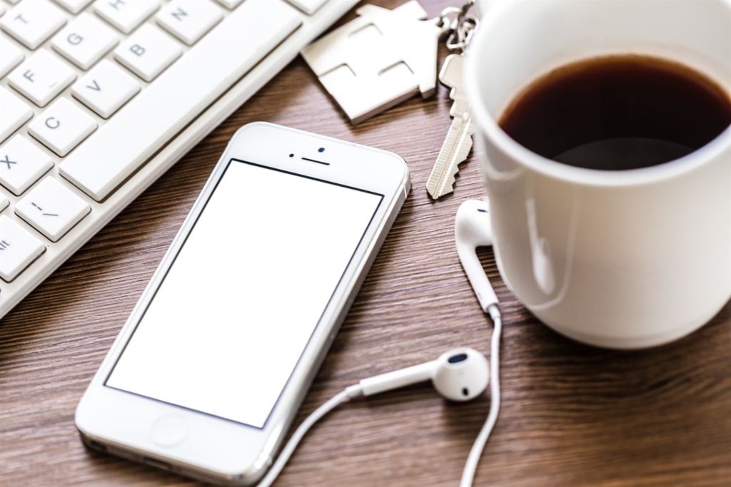 Ein Smartphone mit leerem Bildschirm, Kopfhörern und einer Tasse Kaffee auf einem Holztisch.