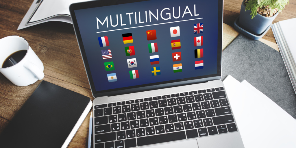 Laptop mit dem Wort 'MULTILINGUAL' und verschiedenen Flaggen auf dem Bildschirm.